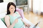 Attractive young woman shopping on-line lying on a sofa at home