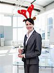 Smiling businesswoman with a novelty Christmas hat drinking Champagne in the office