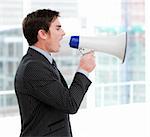 Frustrated businessman yelling through a megaphone standing in the office