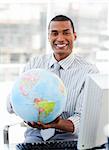 Ethnic businessman holding a terrestrial globe in his office