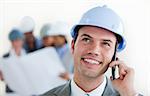 Focus on a male arhitect with a hardhat on phone in front of his team