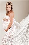 A young pregnant woman is standing semi nude with a sheet lace wrap. Vertical shot.