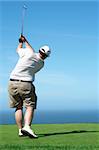 Young male golfer hitting the ball from the tee box next to the ocean on a beautiful summer day