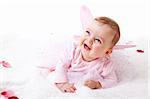 A cute baby girl in fairy wings laughs while lying on the ground covered in flower petals.  Vertical shot.