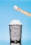 Human trowing a paper to a wastebasket on blue background