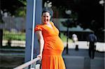 beautiful young happy pregnant woman outdoor in bright nature in orange dress