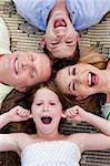 Happy family of four lying on the carpet with their heads together and making fun towards the camera