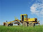 grader on the country road against blue sky