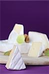 Camembert cheese on cutting board with walnuts and grapes