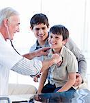 Positive doctor examining a little boy with his father at the practice