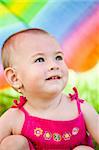 Small baby girl hiding under a big colorful umbrella at a picnic