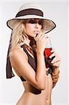 blond and sexy girl in bikini with a summer hat in act to drink a red beverage