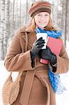 winter street portrait of young beautiful natural looking woman in casual clothes holding books, drinking coffee and smiling