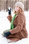 winter portrait of young and beautiful natural looking woman in casual clothes sitting in snow and throwing snowball