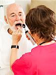 Home healthcare nurse uses a tongue depressor and otoscope to look inside an elderly patient's mouth.