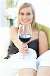 Radiant woman drinking red wine siting on a sofa