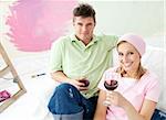 Delighted couple having free time together on a sofa with a glass of wine smiling at the camera