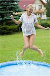 cute blond woman jumping inside a little swimming pool in a garden home