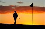 a male golfer goes to remove the flag before he putts at sunrise