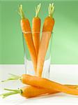 Three carrots in a glass in front of a green background.