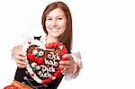 Young happy smiling woman in dirndl dress holding Oktoberfest gingerbread heart. Isolated on white background.