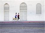Two women running with dog along city street
