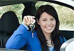 Radiant teenager holding car keys sitting in her new car smiling at the camera