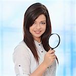 Young attractive smiling business woman looking into a magnifying glass. Over abstract blue background