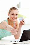 Cute young woman with thumb up holding a card in the living room