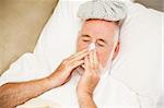 Senior man home sick, blowing his nose.