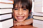 Young boy smiling at camera as he relaxes on table piled up with books