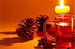 red tea in a glass, cinnamon sticks, star anise and a conifer cone at candle light