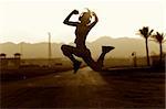 Jumping girl in headphones on a background of road leaving in mountains. Sepia tone.