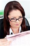 Glowing young businesswoman reading a newspaper in her office with glasses