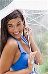 Beautiful young woman smiles towards the camera while holding an umbrella under a spray of water. Vertical shot.