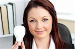 Confident young businesswoman holding a light bulb looking at the camera in her office