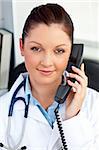 Portrait of an assertive female doctor phoning in her office sitting at her desk