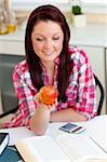 young woman looking at an apple in the kitchen wearing a red shirt