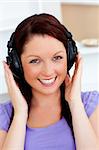 Smiling pretty woman listen to music with headphones looking at the camera at home