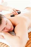 Relaxed young man receiving a back massage with hot stone in a spa center