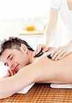 Happy young man enjoying a back massage with hot stone in a spa center