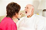 Home nurse uses a thermometer to take an elderly patient's temperature.