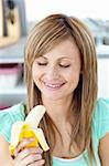 Smiling young woman holding a banana in the kitchen at home