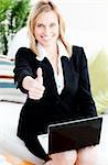 Postive businesswoman with thumb up using her laptop sitting on a sofa