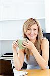 Attractive businesswoman holding a cup using her laptop at her desk