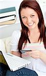 Happy woman with a credit card and a laptop on a sofa at home in the living-room