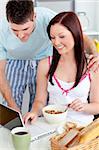 Bright couple using a laptop while breakfast at home in the kitchen