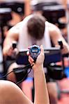 Trainer holding a chronometer while man doing physical exercise on a bicycle in a fitness center