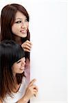 Two attractive young asian women looking at a verical blank sign