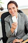 Attractive businesswoman holding a light bulb sitting in her office at her desk